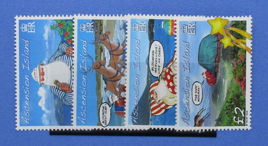 A set of four postage stamps from Ascension Island, displayed side-by-side on a black stand against a solid blue background. The stamps feature colorful cartoon illustrations of Santa Claus and other characters on a blue sky background.