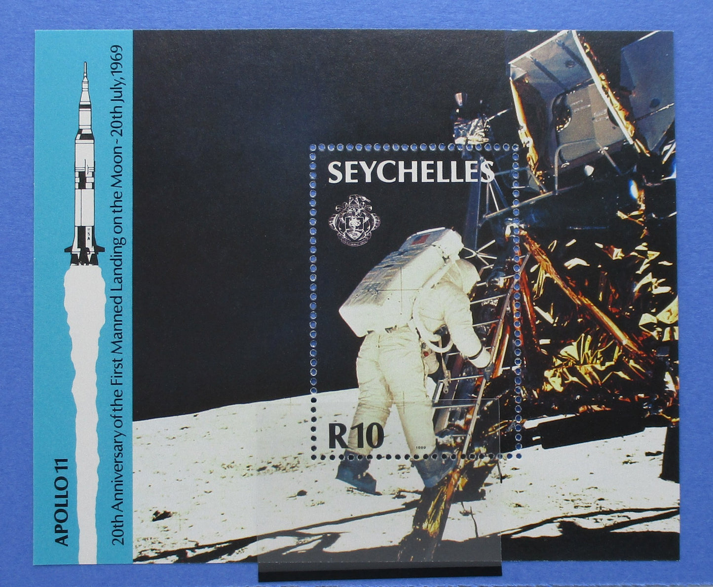 Seychelles Apollo 11 lunar landing postage stamp sheet on a blue background, featuring a spacewalked astronaut, lunar surface, and a blue side panel with a rocket illustration and text.